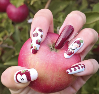 Manicured hand featuring illustrations of apples while holding an apple