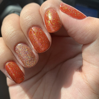 Manicured nails painted in sparkly polish with accents of orange