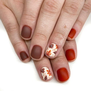 A manicure with solid orange and brown polish and leafpatterned accent nails